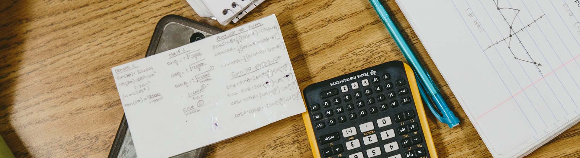 Calculator, pencil, pad of paper and notecard on desk.