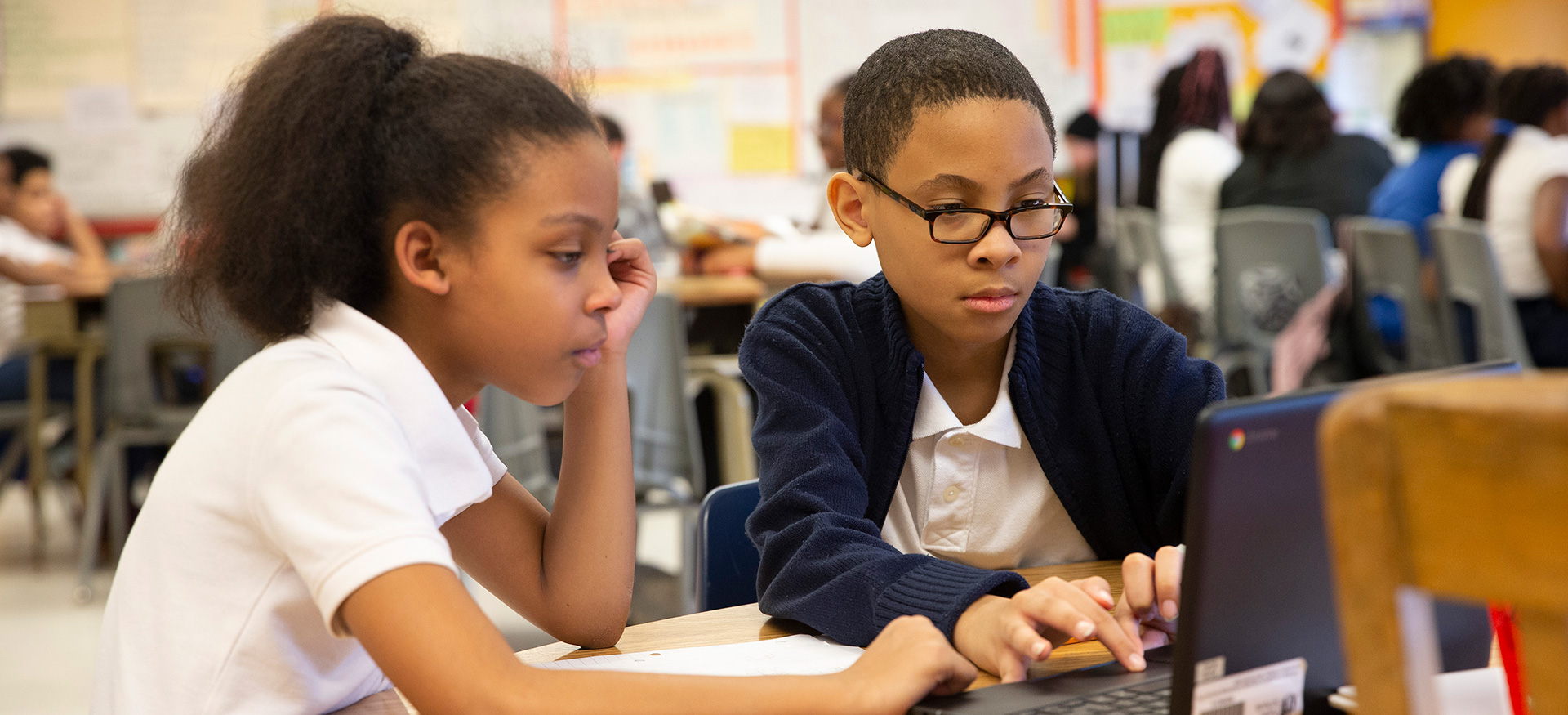 Two students working together on a laptop in a classroom.