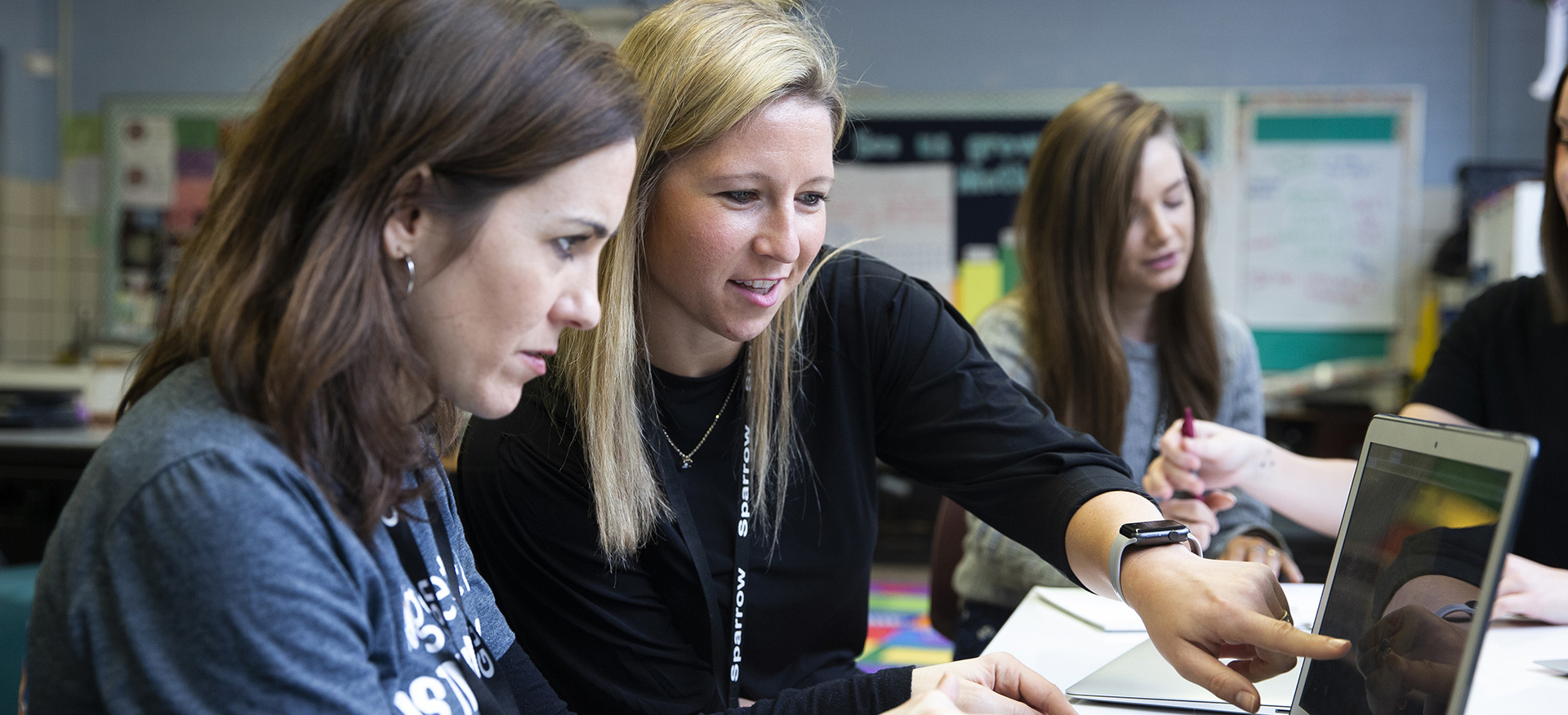 Teacher helping another teacher on a computer.