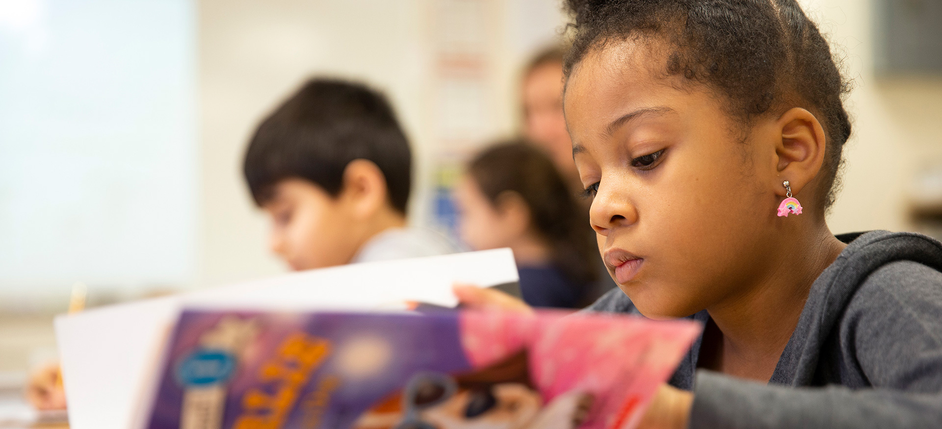 Young student reading quietly at their desk in a classroom.