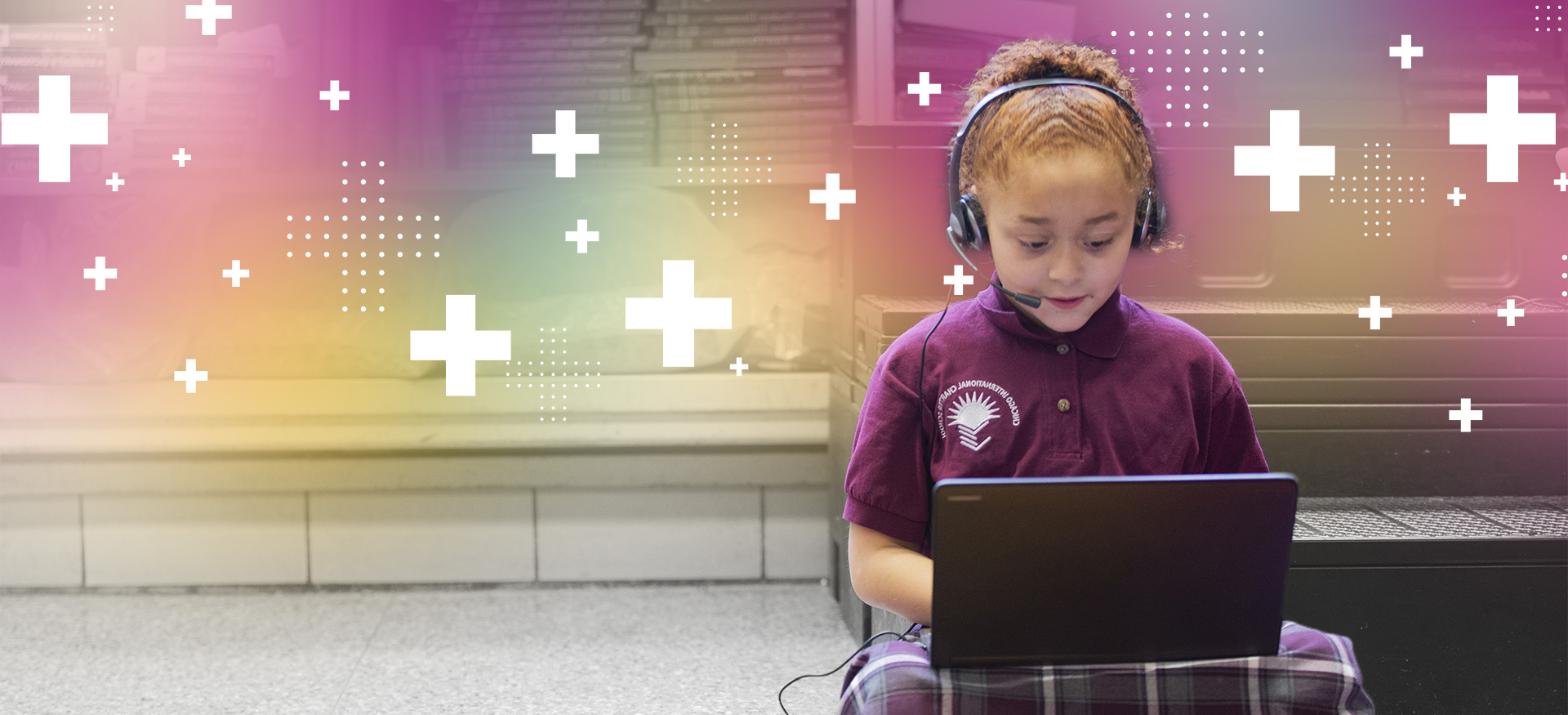 Young student wearing headphones sitting crosslegged on the floor working on a computer.