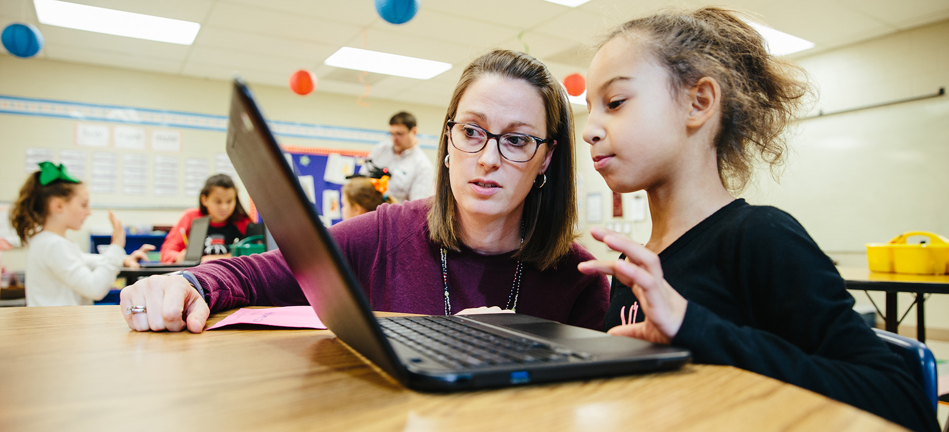 Teacher helping a student who is working on a laptop.