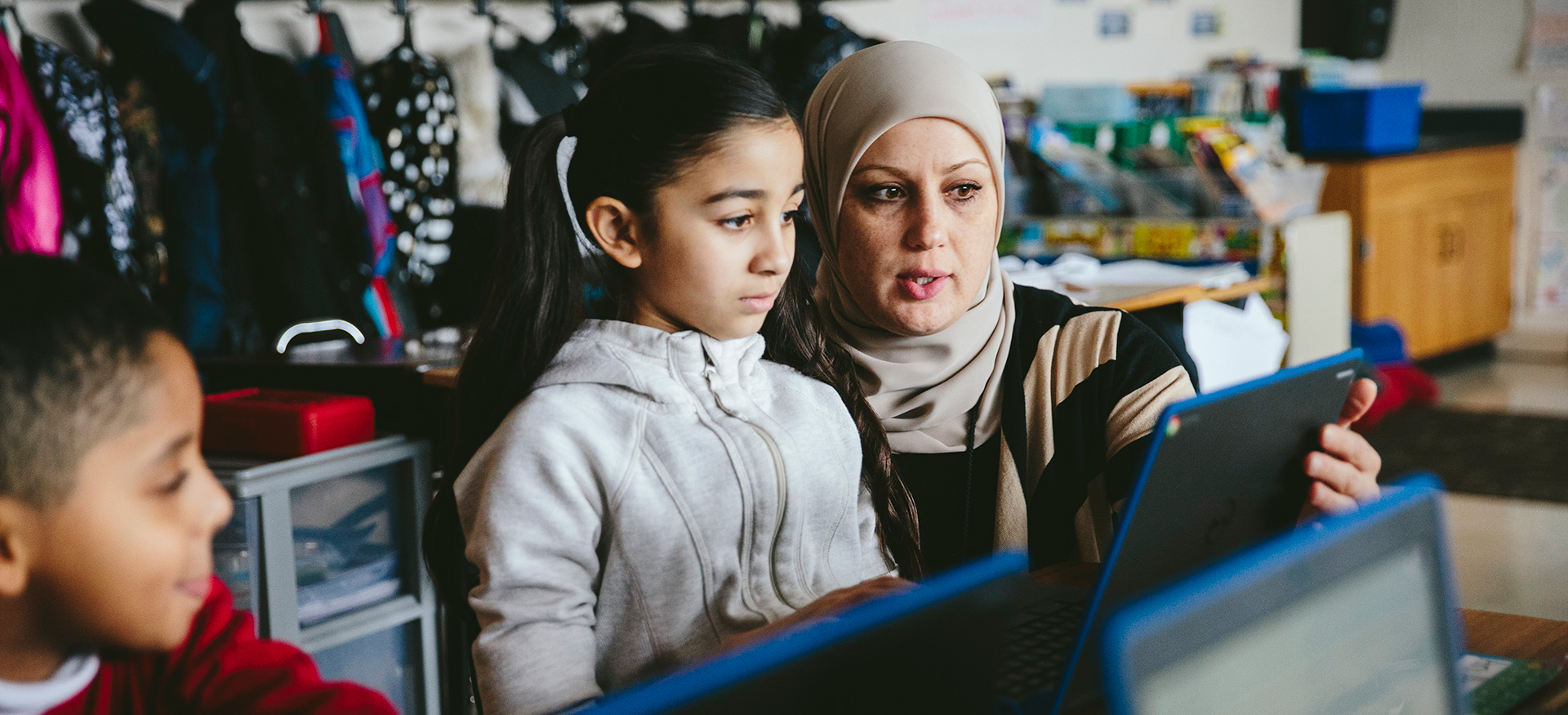 Teacher helping a young student working on a laptop.