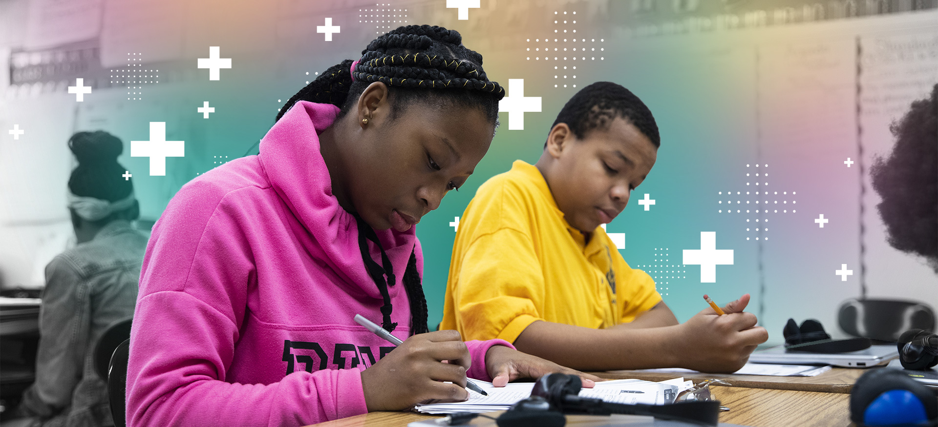 Two students working independently in a classroom and writing at their desks.