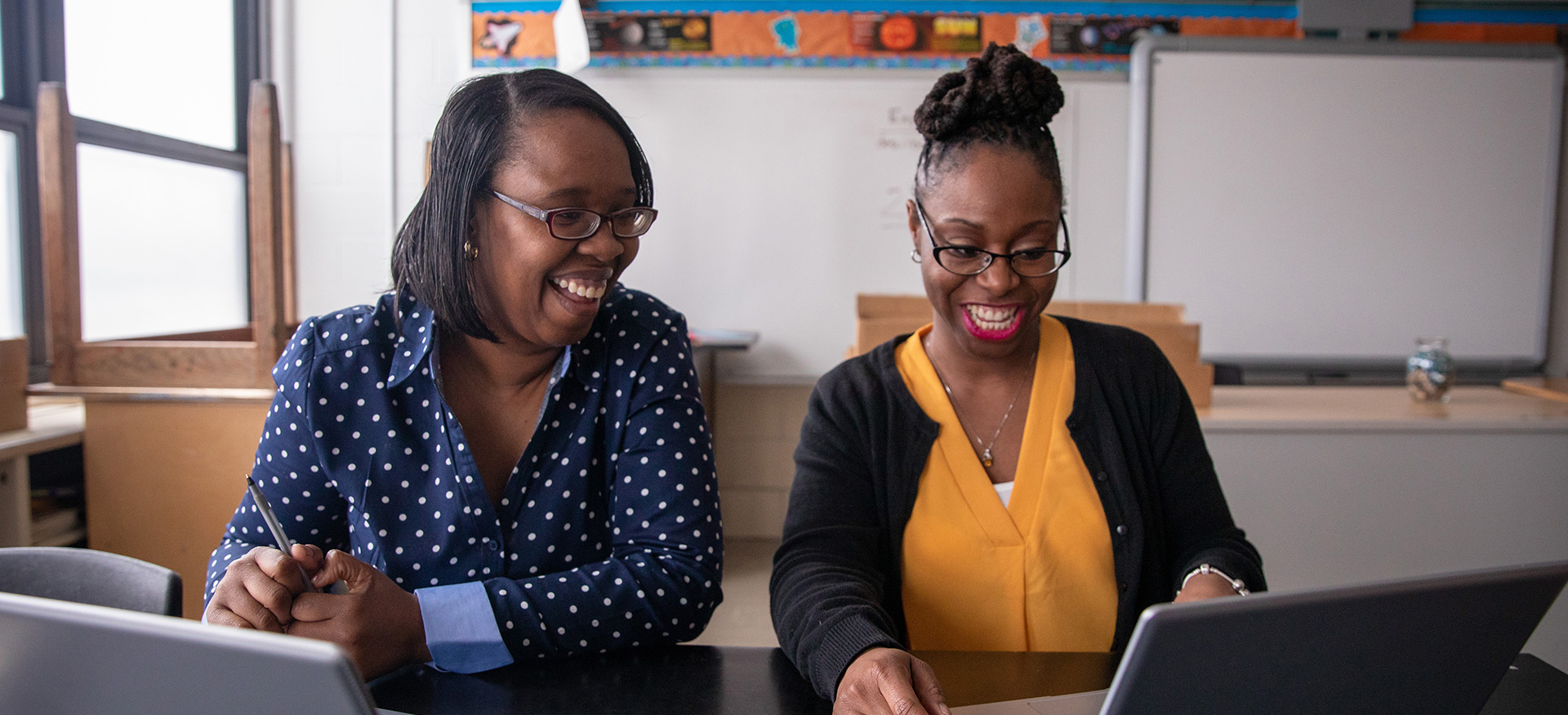 Two educators smiling and laughing working on a computer.