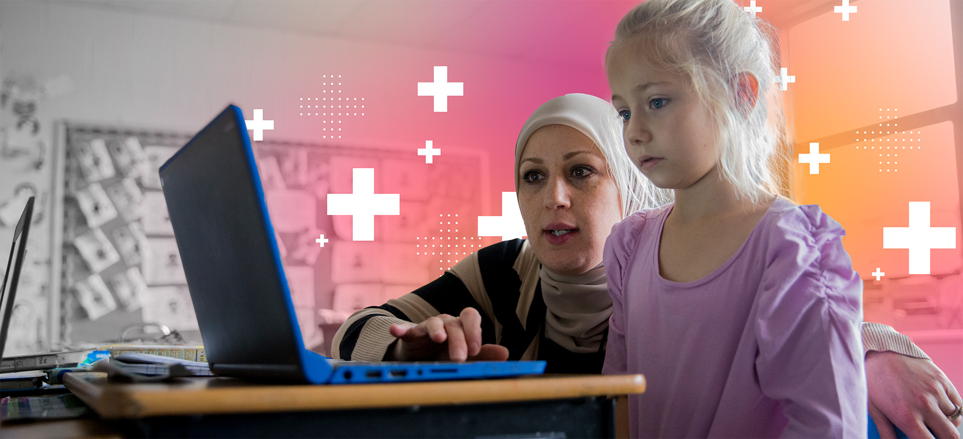 Teacher helping a young student on a computer in a classroom.